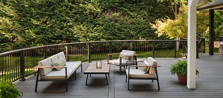 An outdoor seating area on a curved deck with railing, surrounded by evergreen trees
