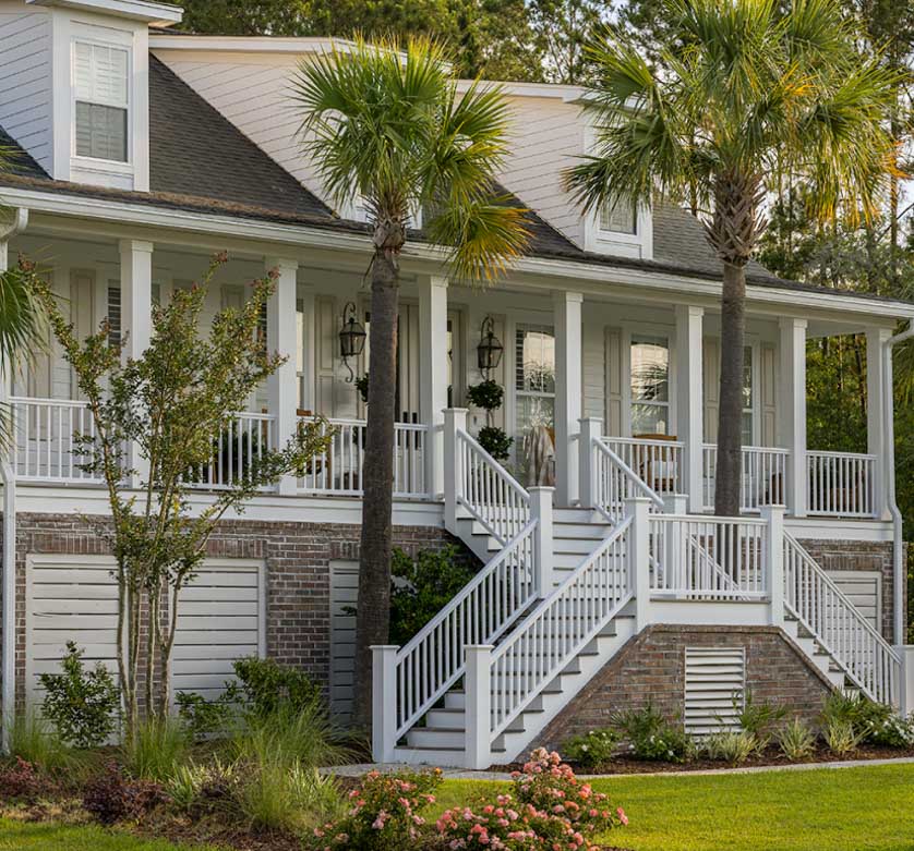 The front of a white and gray home flanked with green palm trees. 