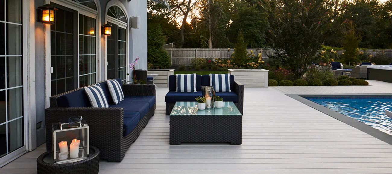 Patio furniture on a tab deck sits opposite to a full glass wall of a house