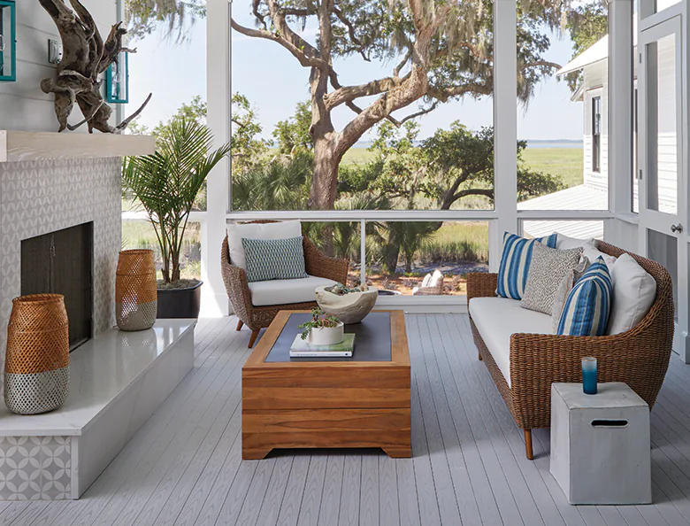 Photo of an enclosed porch with large windows and trees outside that look like they could be in a savannah. The TimberTech porch boards are gray in color with a striking grain pattern.