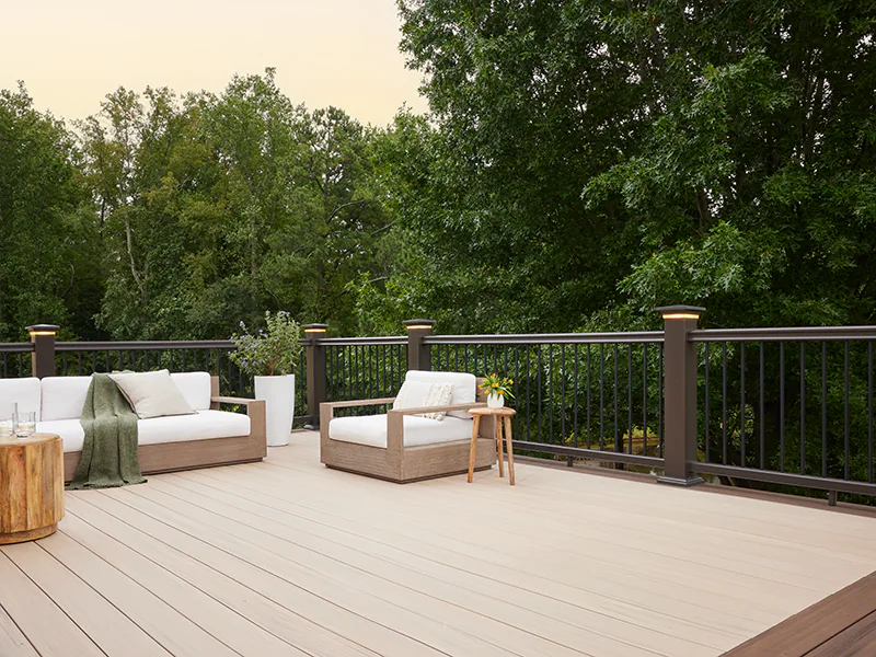 Photo of a light tan TimberTech deck at dusk. Lighted island caps on the deck's railing have turned on and gently illuminate the edges of the deck.