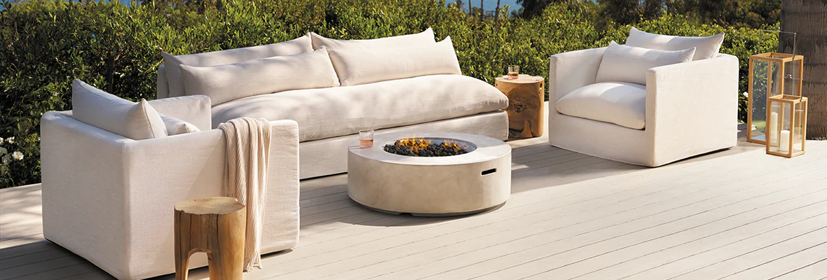 TimberTech deck that is bright, almost white-tan in color with a matching white couch and arm chair set around a modern concrete fireplace in the middle.