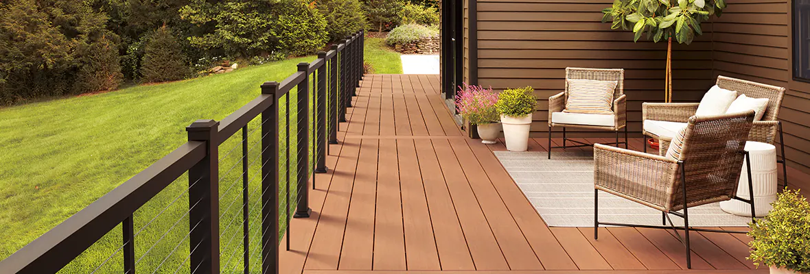 Richly-hued brown deck with red tones and a metal railing with horizontal cable infill running along the side of a home.