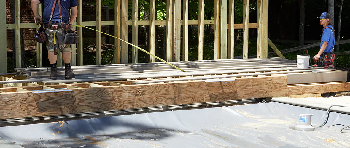 Two contractors follow deck building best practices by inspecting the substructure before installing deck boards.