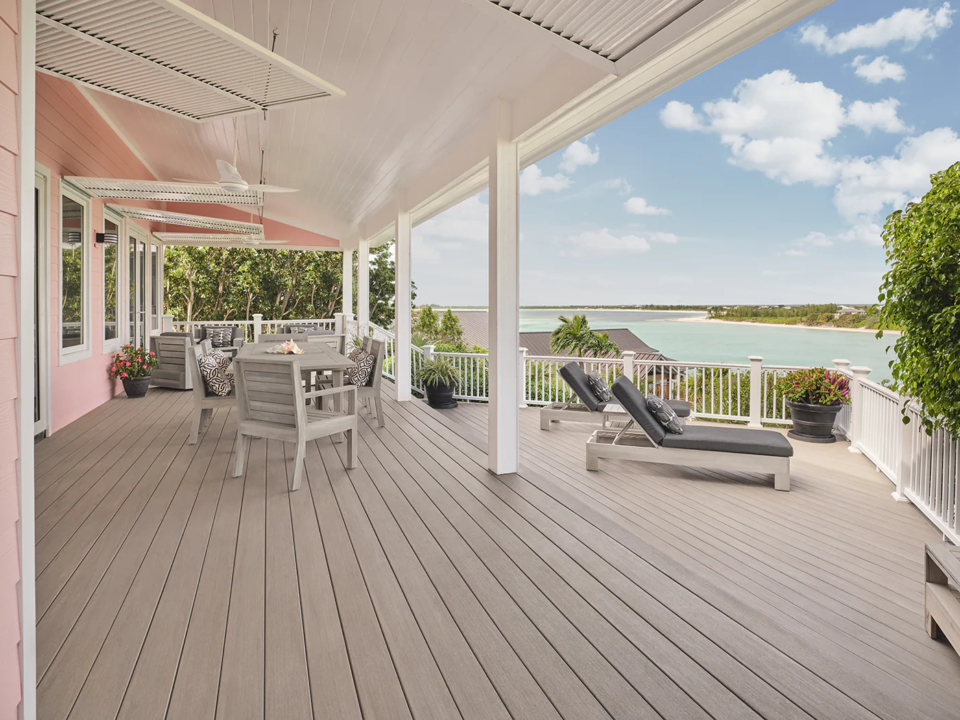 Side view of Darren's light pink house with a light gray deck. The photo is angled towards the view of a tropical bay and landscape.