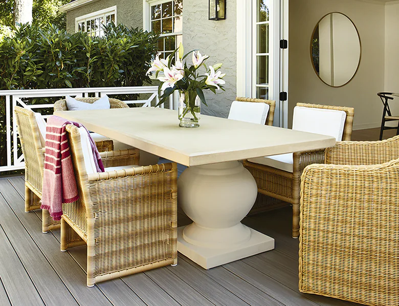 A modern, outdoor dining table with complementary tan wicker chairs is set up on the gray deck