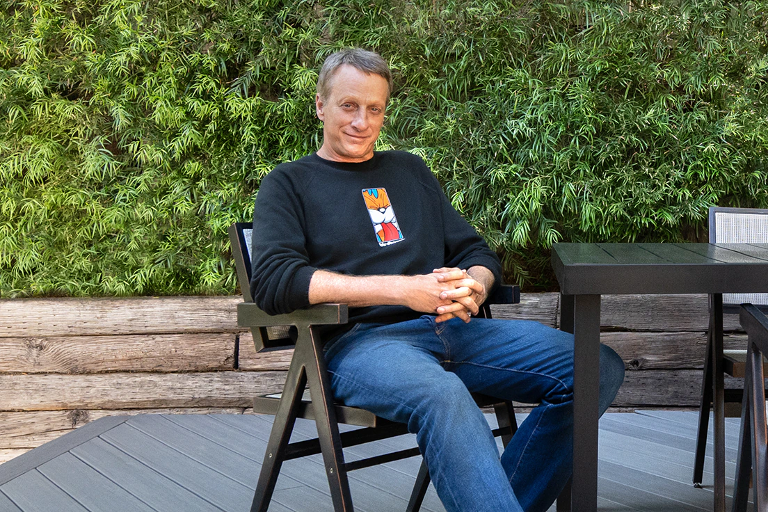 Tony Hawk folds his hands and smiles while sitting in a chair on his new deck.