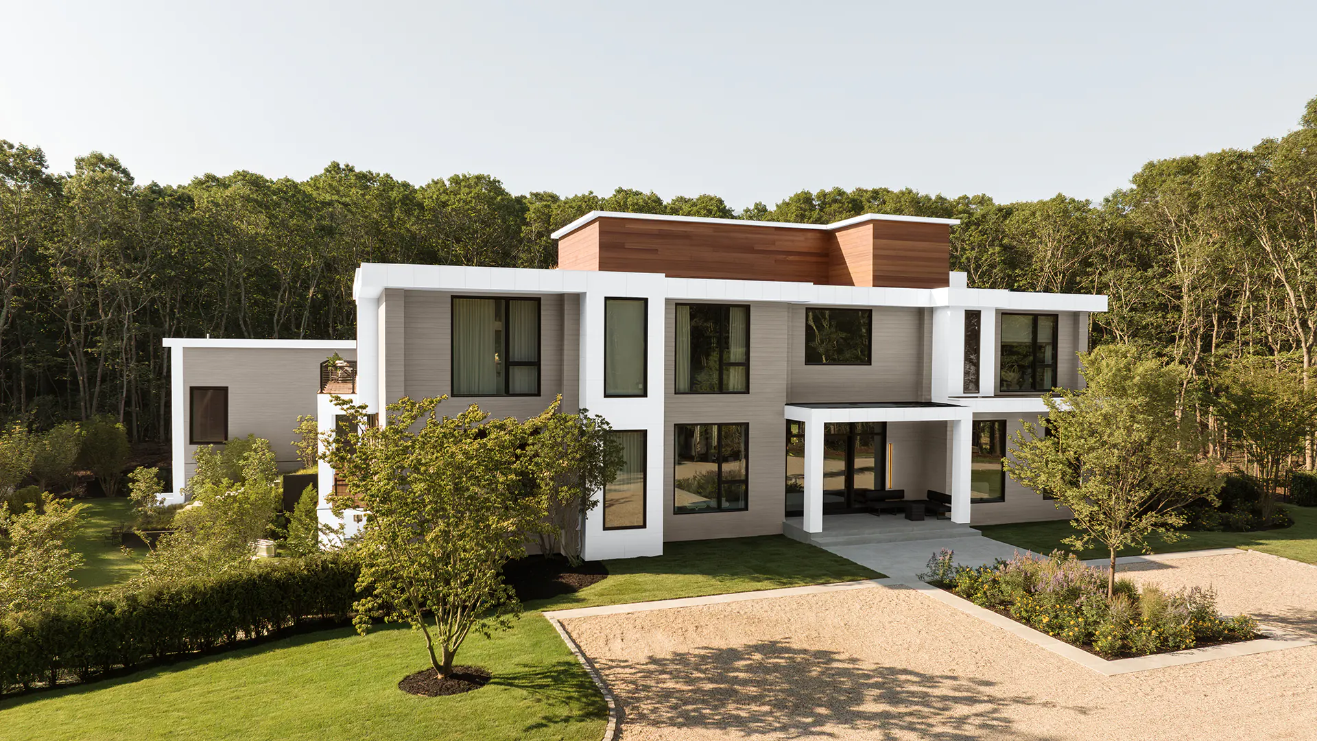 Angled side view of a large, contemporary home outside of New York. Light gray cladding with a blended wood grain is on the outside of the house and real wood cladding is used on the third story of the building.