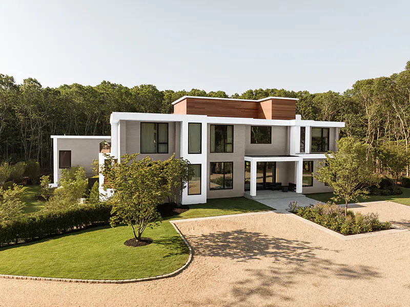 Large, modern home on a property surrounded by trees.